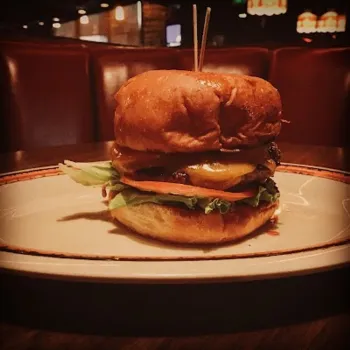 A cheeseburger with lettuce, tomato, and cheese on a toasted bun is served on a plate in a dimly lit restaurant booth.