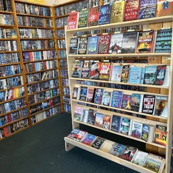 Bookshelves and a central display rack filled with various fiction and non-fiction books in a well-organized bookstore.