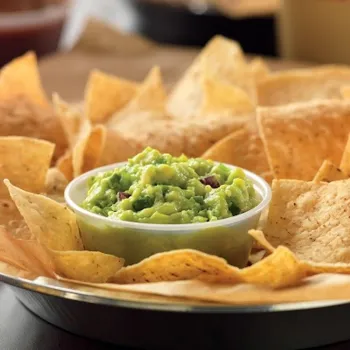 A small bowl of guacamole surrounded by crispy tortilla chips on a round metal tray.