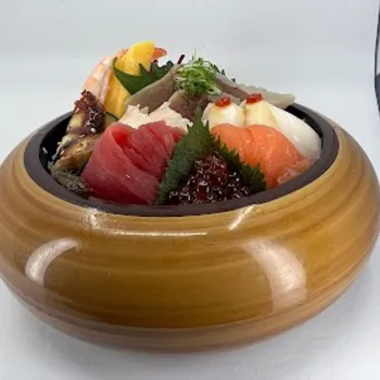 A wooden bowl filled with assorted sashimi, including salmon, tuna, shrimp, roe, leafy garnishes, and lemon, against a white background.