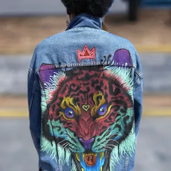 Person with an afro wearing a denim jacket featuring a colorful, painted roaring leopard face and a red crown symbol on the back.