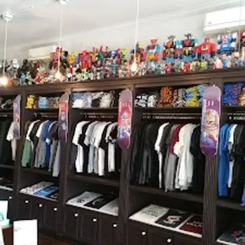 Clothing store interior with neatly organized racks of t-shirts, shelves displaying folded shirts, and toy figures arranged on top of the cabinets.