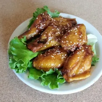 A plate of glazed chicken wings garnished with sesame seeds, served on a bed of green lettuce.