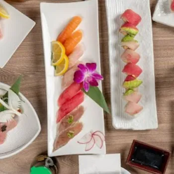 Assorted sushi and sashimi plates arranged on a wooden table, accompanied by soy sauce, wasabi, and a small sake bottle.
