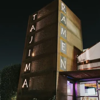 A tall, illuminated sign reading "TAJIMA RAMEN" stands outside a restaurant at night.