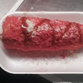A corn on the cob covered with red seasoning and drizzled with sauce, served on a white foam tray with a wooden stick.