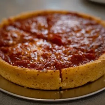 A deep-dish pizza with a thick golden crust and tomato sauce on top, sliced into four pieces, served on a round metal tray.