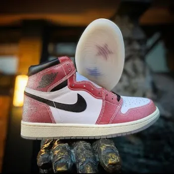 A pair of red, white, and black high-top sneakers with a visible Nike swoosh, displayed on a textured surface with one shoe standing upright and the other showing its translucent sole.