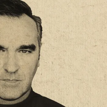 A black-and-white portrait of a man with dark hair, thick eyebrows, and a serious expression, set against a textured beige background.