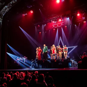 Performers stand on a lit stage in front of an audience, with red lighting and a large star shape illuminated in the background.