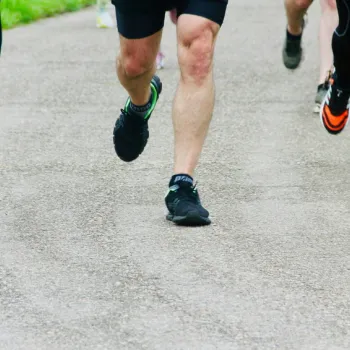 Four runners in athletic clothing run on a paved outdoor path; only their legs and feet are visible.