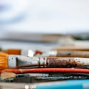 A close-up view of several well-used paintbrushes, some with paint stains, lying horizontally on a surface.