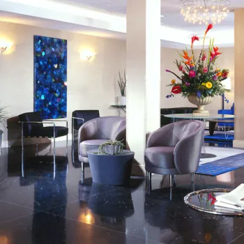 Modern hotel lobby with black tile floor, contemporary chairs, a large floral arrangement, abstract artwork, and glass coffee tables.