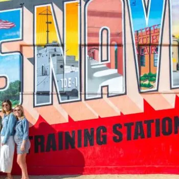 A group of five people poses for a photo in front of a large colorful mural reading "U.S. Naval Training Station.