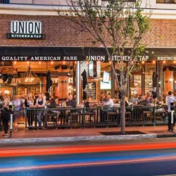 Street view of Union Kitchen & Tap with outdoor diners, illuminated signs, and blurred car lights passing by in the evening.