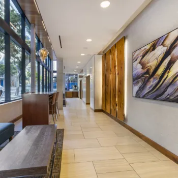 Modern lobby with large windows, contemporary furniture, a wooden accent wall, and abstract artwork. Street view visible through the glass.