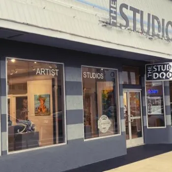 Exterior view of The Studio Door art gallery and artist studios, with large display windows and sidewalk, in an urban street setting.