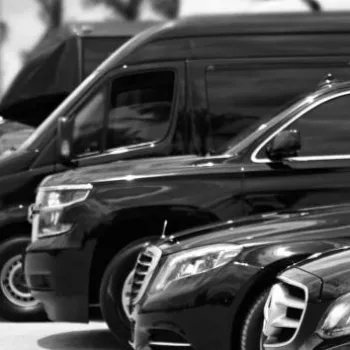 A row of black luxury vehicles, including sedans and vans, parked outdoors with a person in a suit standing in the foreground.