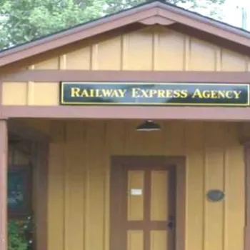 Small wooden building with a sign reading "Railway Express Agency" above the door, located near a street and railroad tracks.