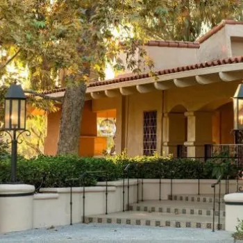 Entrance to a Mediterranean-style building with tiled roof, surrounded by greenery and two decorative lanterns; a sign reads "Avant.