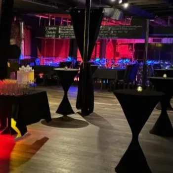 Dimly lit event space with cocktail tables, a black sofa, glasses set on a side table, and blue and red lighting in the background.