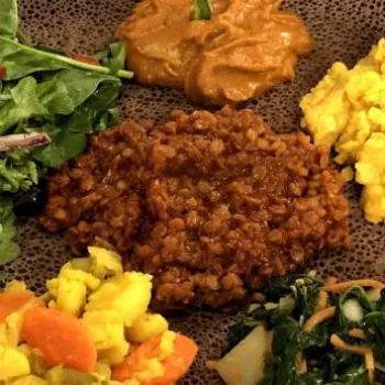 A plate of Ethiopian food featuring injera bread topped with various vegetable stews, salad, and legume dishes arranged in separate portions.