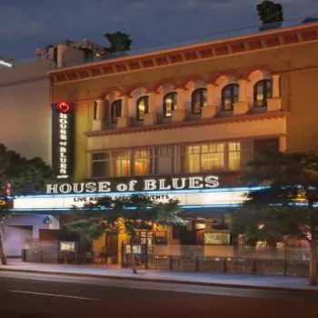 Street view of the House of Blues building at dusk, with illuminated signs and storefronts, and trees lining the sidewalk.