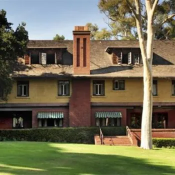 A large, historic two-story house with brick and stucco exterior, several windows, green awnings, and a well-kept lawn in front.