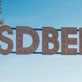 A large metal sign displays the hashtag "#SDBEER" against a clear blue sky, with part of a tree visible on the left.