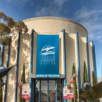 The entrance of the San Diego Air & Space Museum, featuring large aircraft displays on either side of the main doors and a blue banner above the entrance.