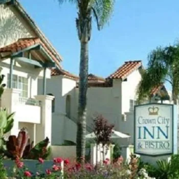 A two-story building with red-tiled roofs and palm trees houses the Crown City Inn & Bistro, indicated by a sign in the landscaped front garden.