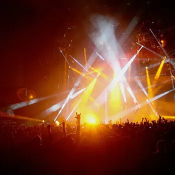 Crowd watching a concert indoors with bright stage lights and colorful beams illuminating the performers.