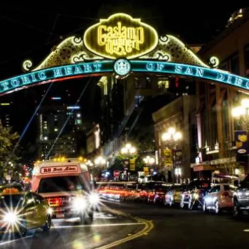 Cars drive under the illuminated Gaslamp Quarter sign at night on a busy street in downtown San Diego, with buildings and streetlights visible.