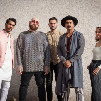 Five people stand side by side against a textured wall, wearing a mix of modern and traditional clothing, looking directly at the camera.
