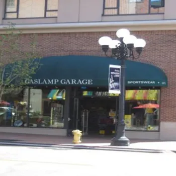 Street view of a brick building with green awnings reading "GASLAMP GARAGE" and "SPORTSWEAR," displaying various items in the windows.