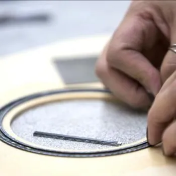 Close-up of hands installing decorative inlay around the soundhole of an acoustic guitar body.