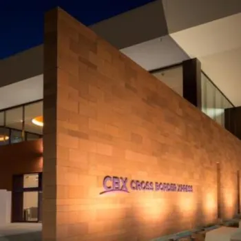 Modern building with tan stone exterior and large overhang at night, labeled "CBX Cross Border Xpress" in purple letters on the wall.