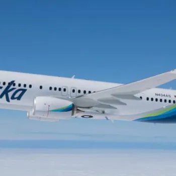 An Alaska Airlines plane flies above the clouds, featuring the airline's logo and a stylized face on the tail fin.