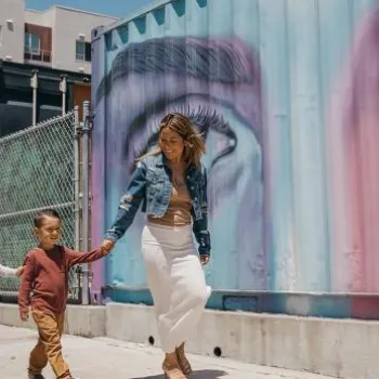 A family of four walks together on a sidewalk next to a building with colorful eye-themed mural art.
