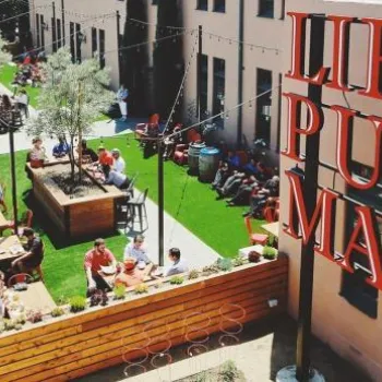Outdoor seating area at Liberty Public Market with people dining at tables beside a large building and greenery during the day.