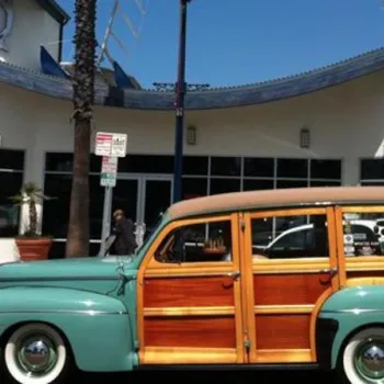 A vintage wood-paneled station wagon is parked in front of the California Surf Museum building on a sunny day.