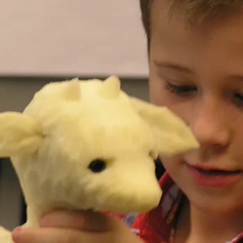 A young boy holds and looks at a cream-colored plush toy animal with small horns and black eyes.