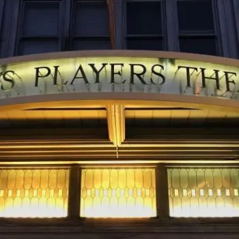 Exterior view of Lamb's Players Theatre entrance with illuminated sign and decorative glass windows.