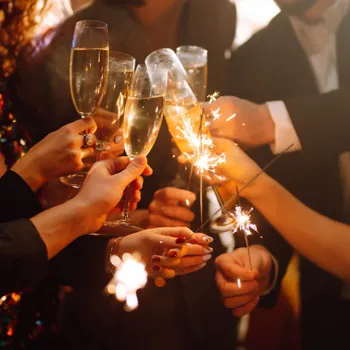 Group of people holding champagne glasses and sparklers, raising a toast in celebration.