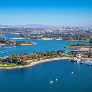 Aerial view of Mission Bay in San Diego, showing green parks, marinas, boats on the water, and the city skyline in the distance under a clear blue sky.