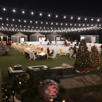 Outdoor skating rink at night with people skating, string lights overhead, holiday decorations, Christmas trees, and seating areas with fire pits.