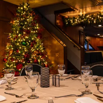 A dining table set for six is in the foreground, with a decorated Christmas tree and festive garland with lights visible in the background.
