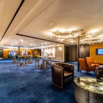 A spacious, modern lounge area with blue carpet, leather chairs, high tables, and contemporary lighting fixtures.