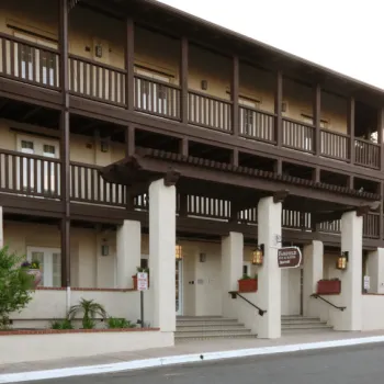 Two-story hotel building with brown wooden railings, beige walls, and a sign reading "Fairfield Inn & Suites" above the entrance. Steps lead up to the front doors.