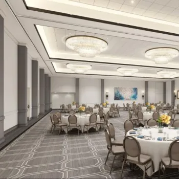 Spacious banquet hall with round tables set for an event, neutral decor, large chandeliers, and modern wall art.